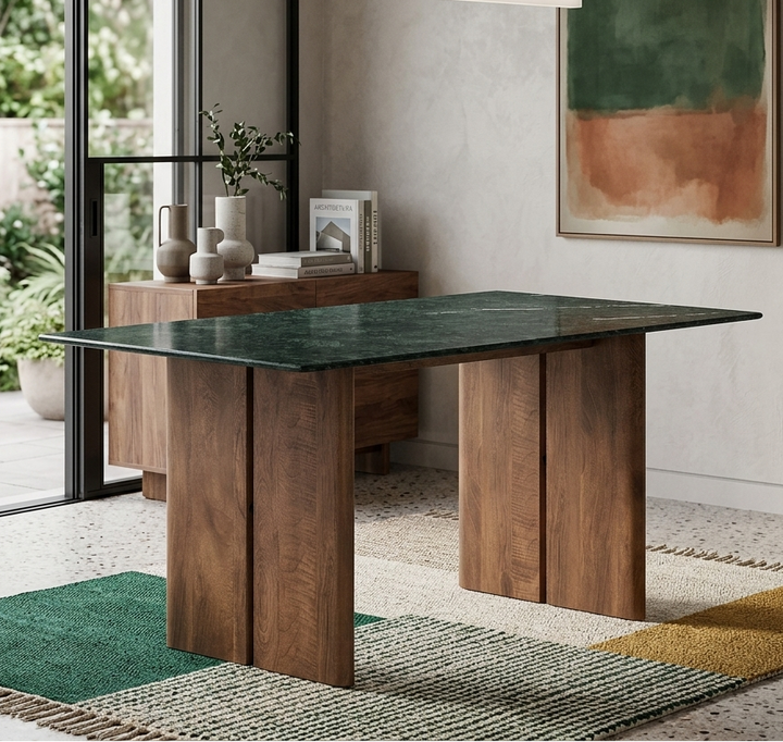 Modern dining table with wooden legs and green marble top in a room with large windows and a painting on the wall.